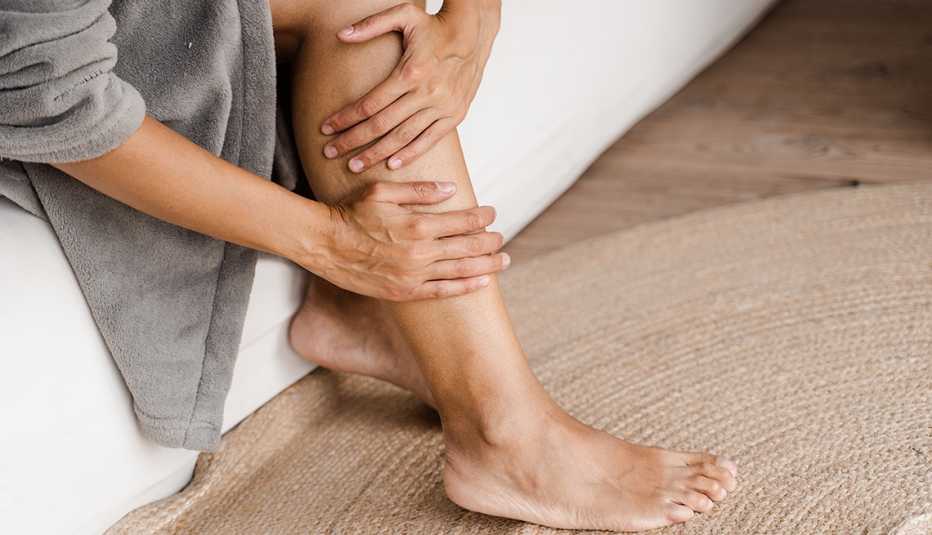 Una mujer, sentada en un sofá, se masajea una de sus piernas