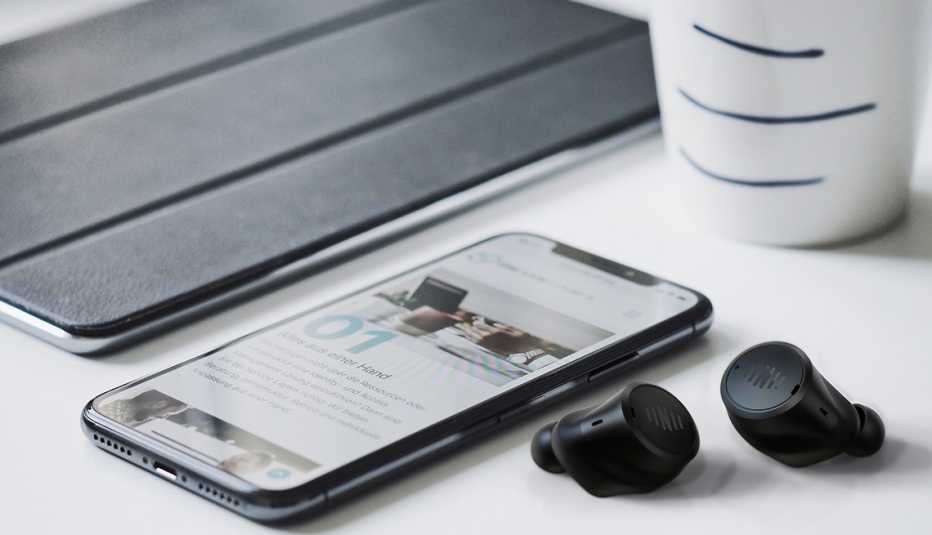 Audífonos recargables de Nuheara, un teléfono celular y una taza sobre un escritorio