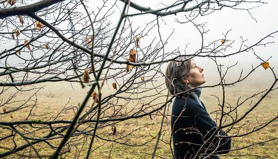 Mujer afuera cerca de un árbol en un día sombrío de otoño con cara de tristeza