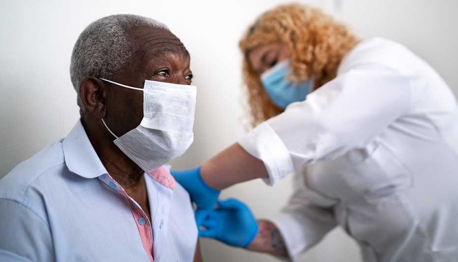 Enfermera vacuna en el brazo a hombre con mascarilla