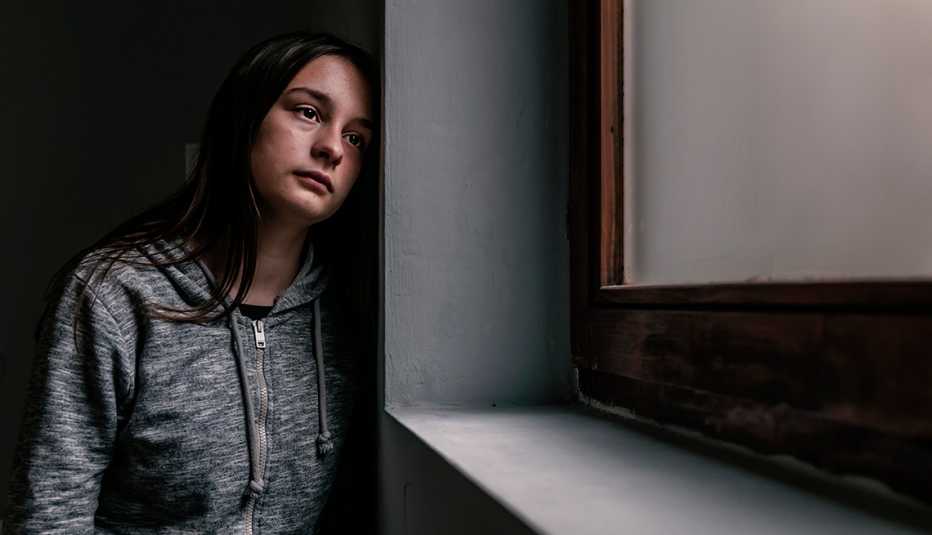 Mujer joven luce triste mientras mira por una ventana