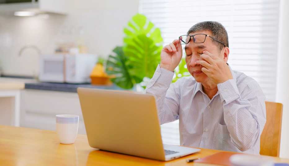 Un hombre se masajea un ojo mientras trabaja frente a una computadora