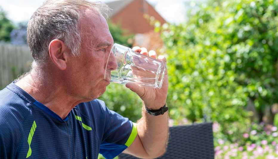 Un hombre toma un vaso de agua sentado en su patio