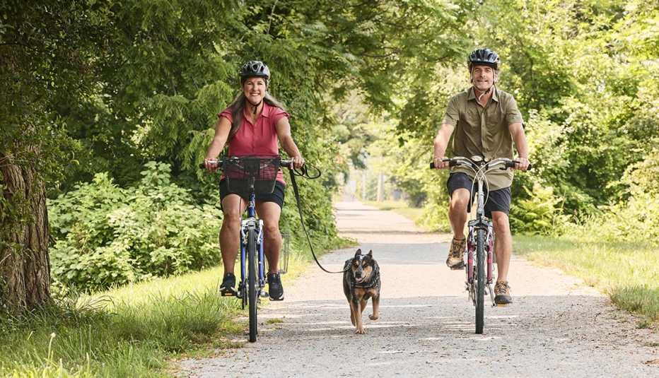 Lori Miller anda en bicicleta por un parque con su pareja y su perro