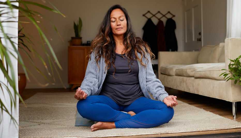 Una mujer practica la meditación sentada en el piso de su sala
