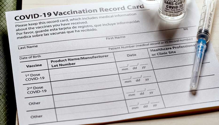 Tarjeta de vacunación contra la Covid-19, una jeringa y un vial.