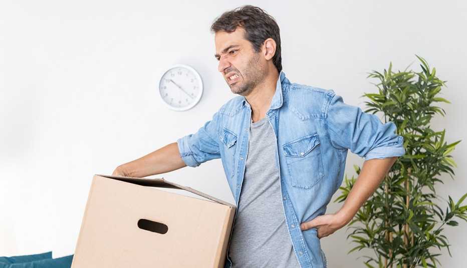 Un hombre carga una caja y hace un mal movimiento que le provoca dolor