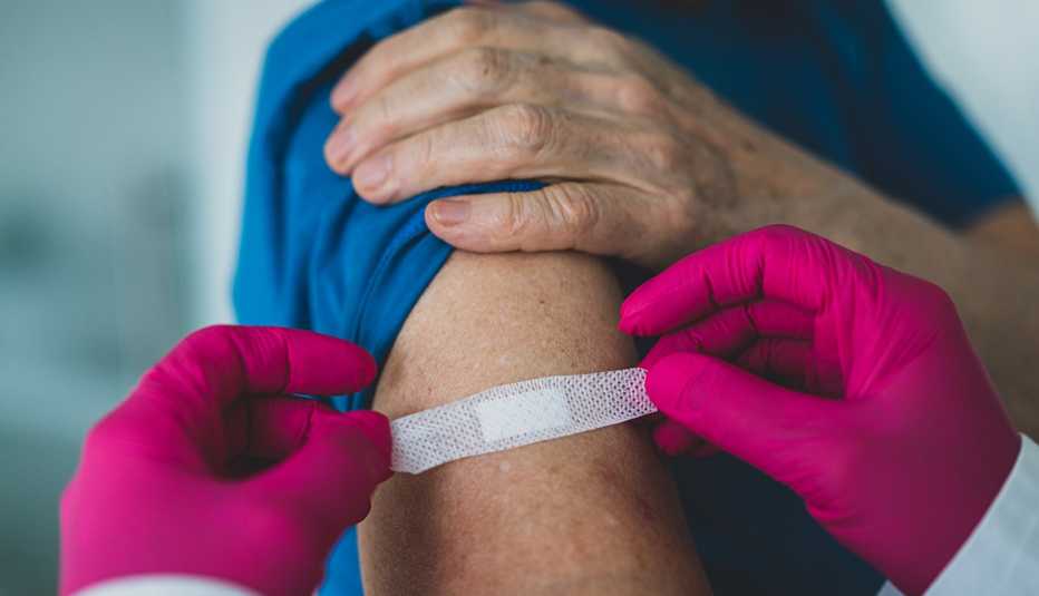 Un doctor coloca una curita en el brazo de una persona luego de vacunarla