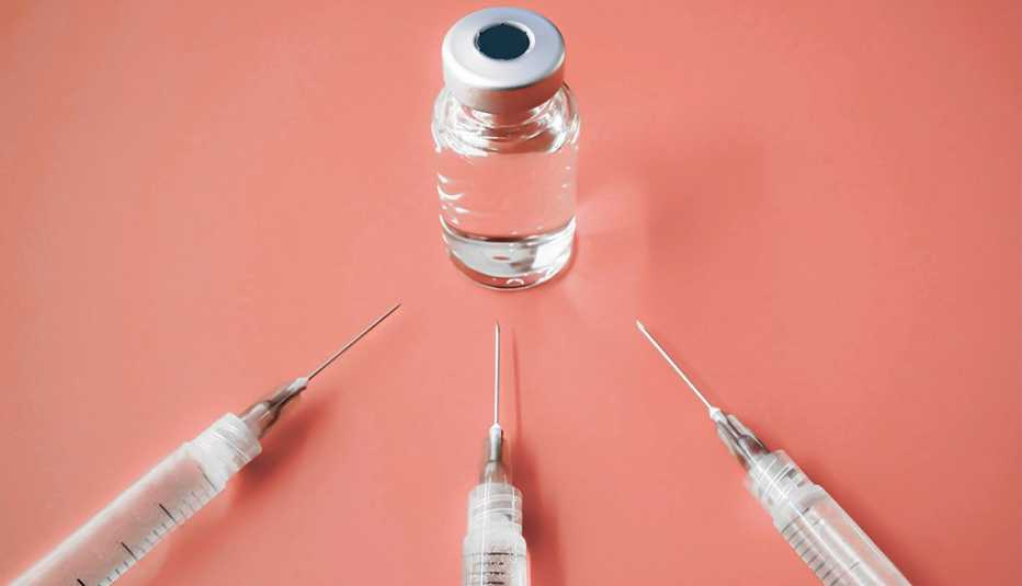 Tres jeringuillas y un frasco de una vacuna sobre un fondo color durazno