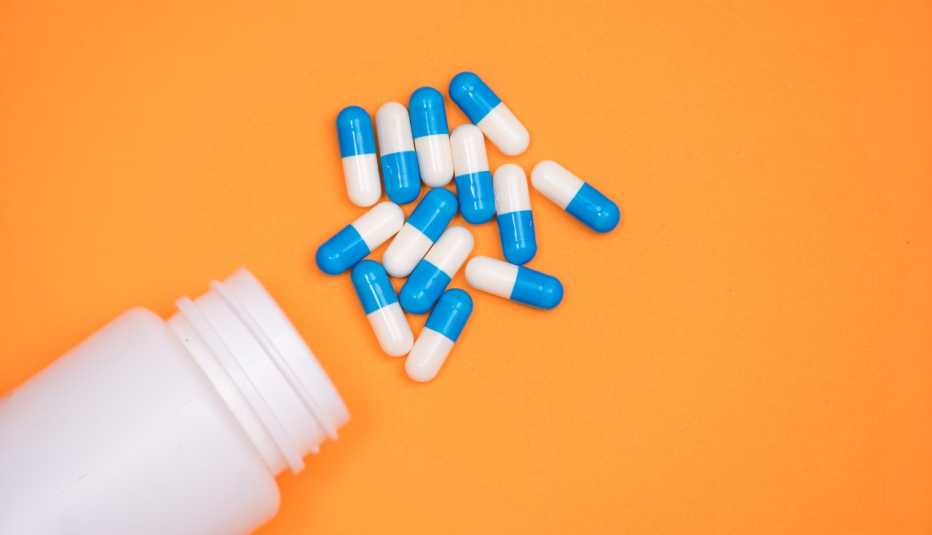 Frasco de antibióticos derramado y cápsulas blancas y azul sobre un fondo amarillo naranja