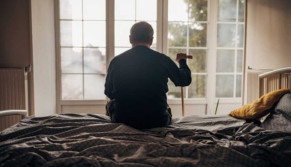 Un hombre solo sentado en su cama y mirando por una ventana