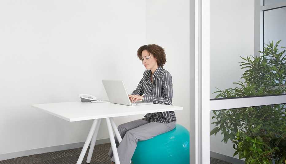 Mujer usando una computadora sentada en una bola de ejercicios 