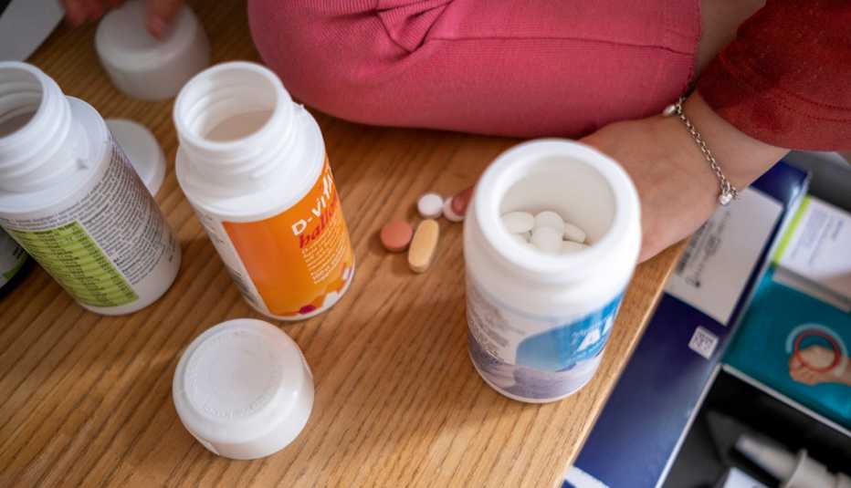 Varias botellas de suplementos sobre una mesa y la mano de una mujer alcanza una pastilla