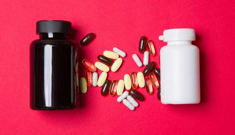 Dos potes de medicinas, uno negro y otro blanco y entre medio pastillas de varios colores y tamaños sobre un fondo rojizo