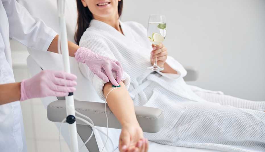 Una mujer recibe una infusión intravenosa mientras sostiene una copa de agua con lima
