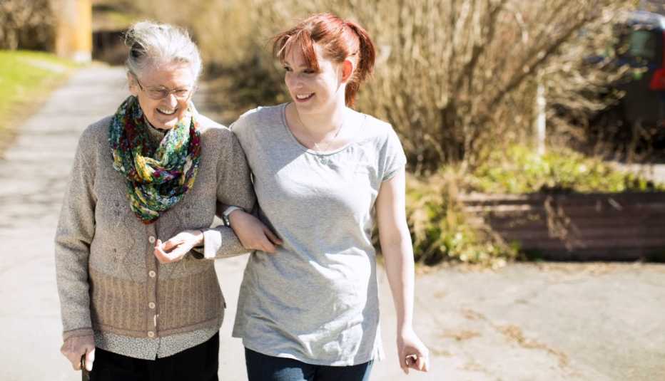 Una mujer mayor que camina con la ayuda de un cuidadora.