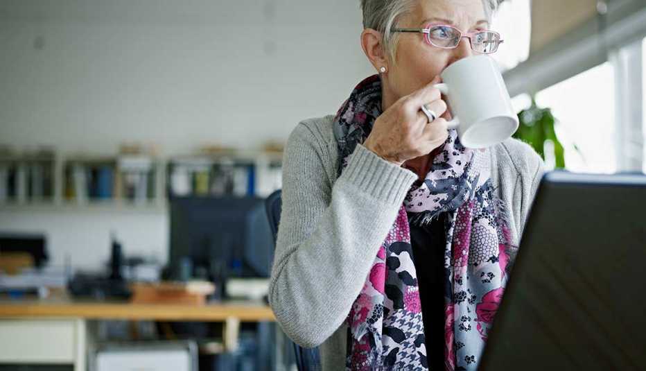 Mujer tomando una taza de café frente a su computadora