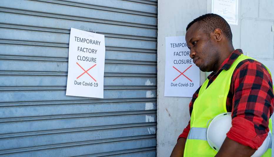 Un obrero mira una puerta cerrada con un letrero que dice 'cerrado temporeramente por COVID-19'