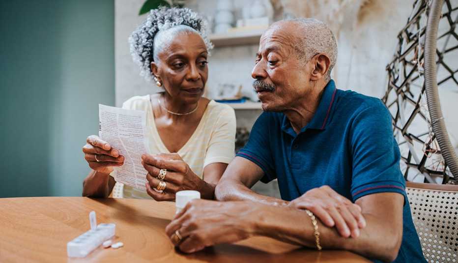 Una pareja mayor revisa una lista de medicamentos en su casa