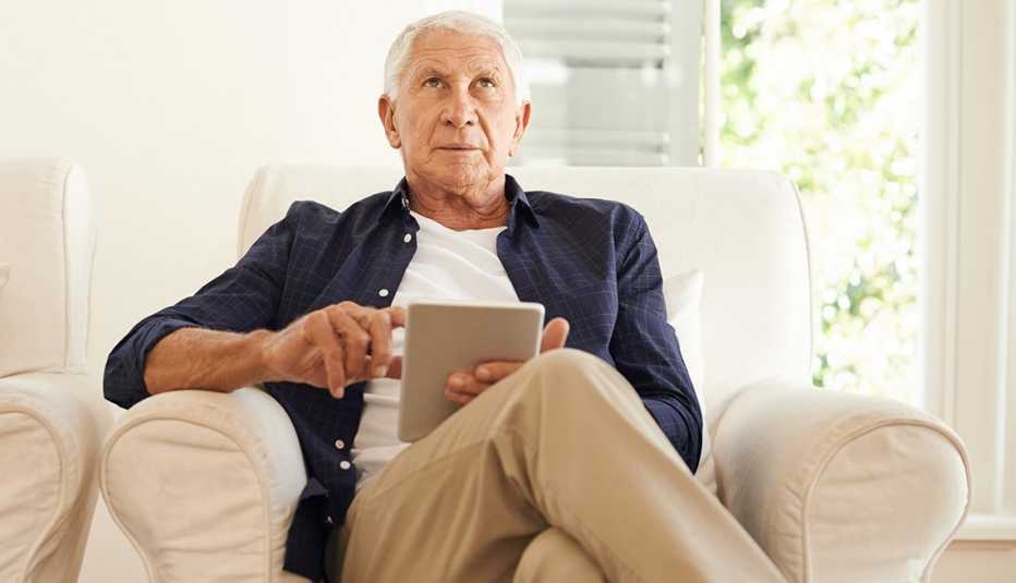 Hombre mayor sentado tratando de recordar algo mientras usa una tableta