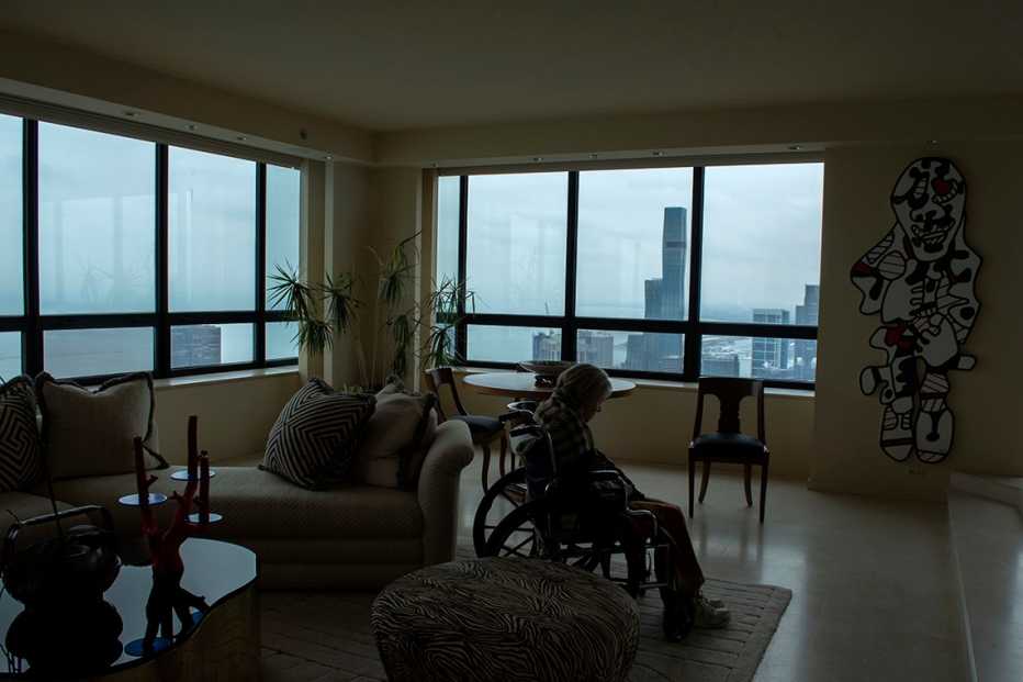 Retrato de una mujer mayor en silla de ruedas en una habitación grande en un edificio de gran altura con vistas a la ciudad