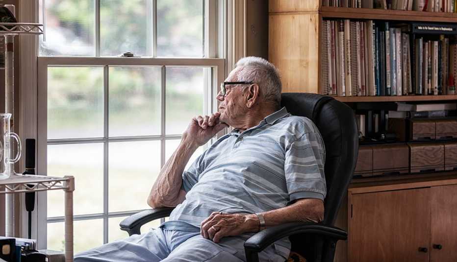 Un hombre mayor sentado en una silla mira por una ventana