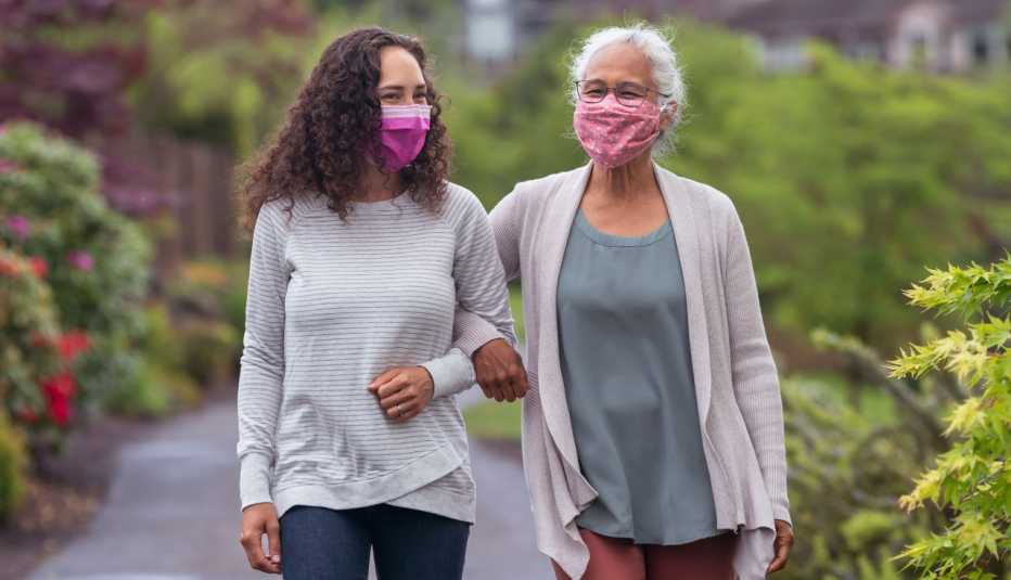 Dos mujeres, usando mascarillas, caminan al aire libre