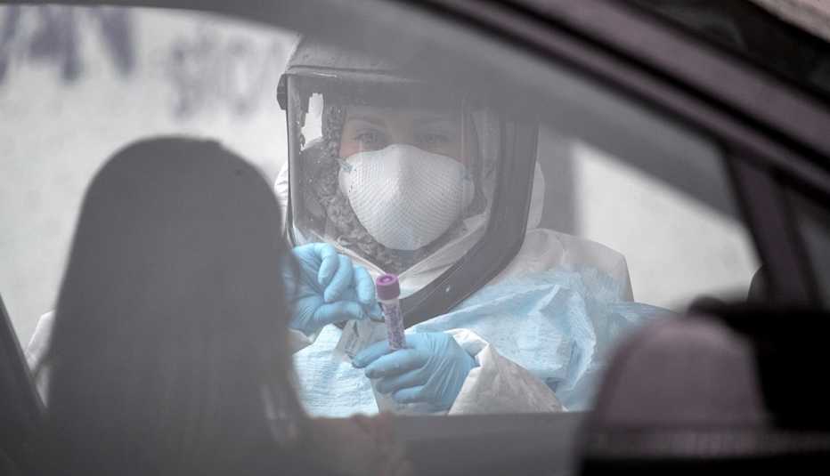 Una enfermera con uniforme protector examina a una persona en su auto