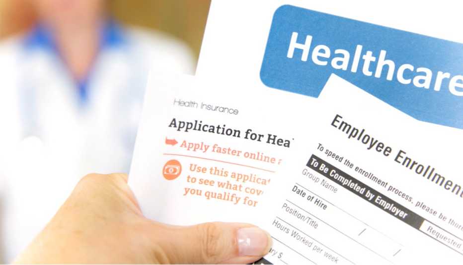Una mano sostiene varios formularios de solicitud de planes médicos
