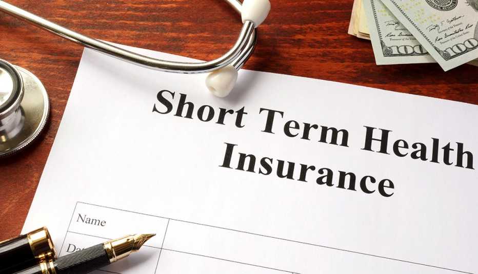 Documento sobre planes de seguro a corto plazo, un estetoscopio, dinero y un bolígrafo sobre un escritorio