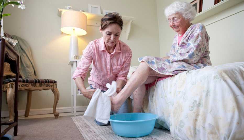 Un cuidador lava los pies de una mujer mayor.