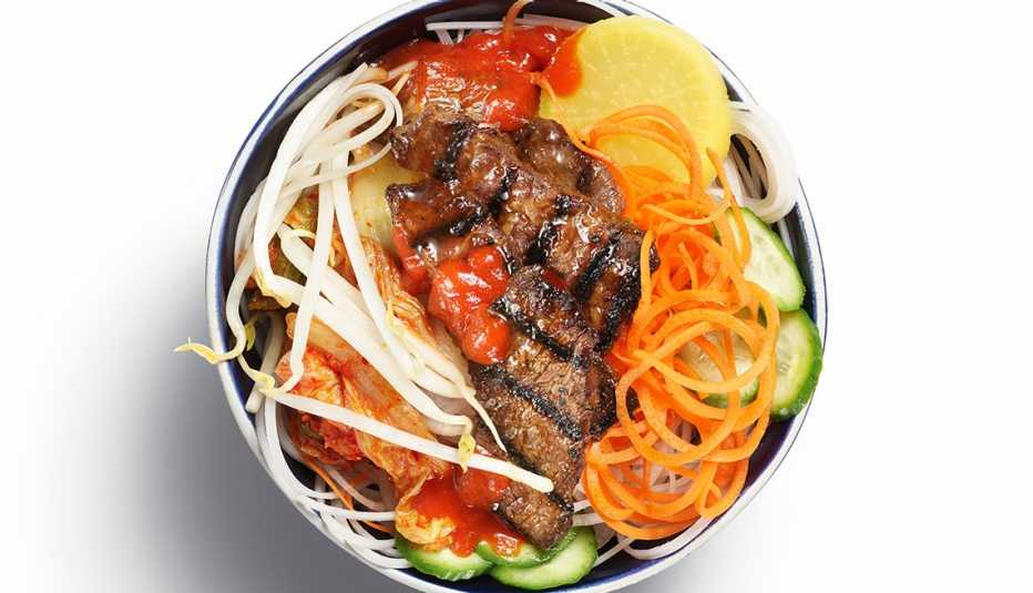 Plato de comida coreana con carne asada, verduras y fideos