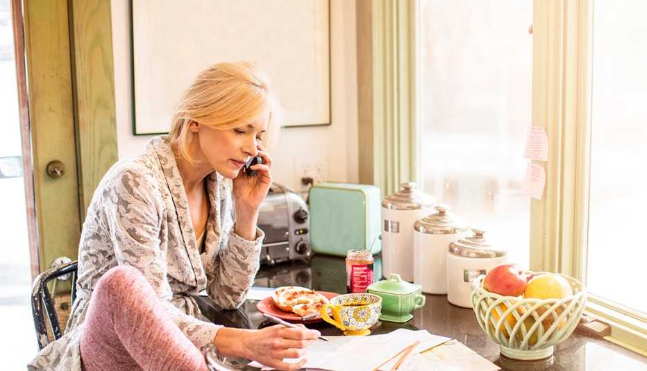 Una mujer en su cocina paga sus facturas por teléfono