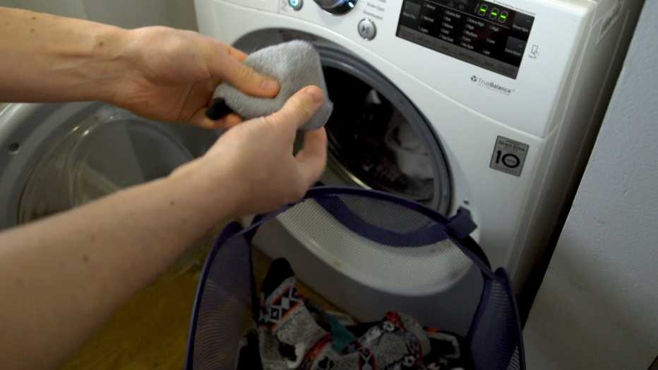 Manos de una persona coloca ropa sucia en una lavadora