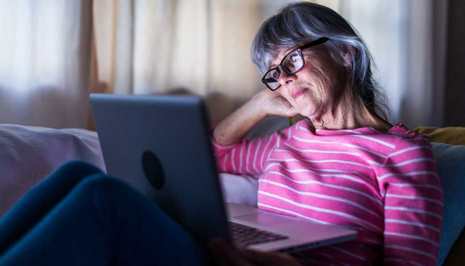 Una mujer mira su computadora portátil sentada en un sofá