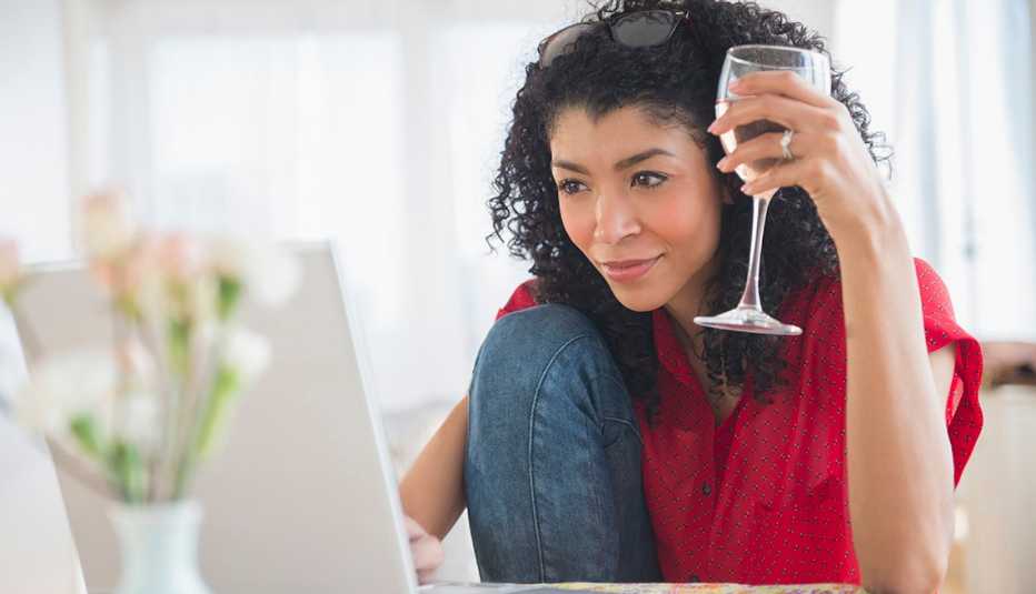 Una mujer toma una copa de vino mientras hace una búsqueda en su computadora
