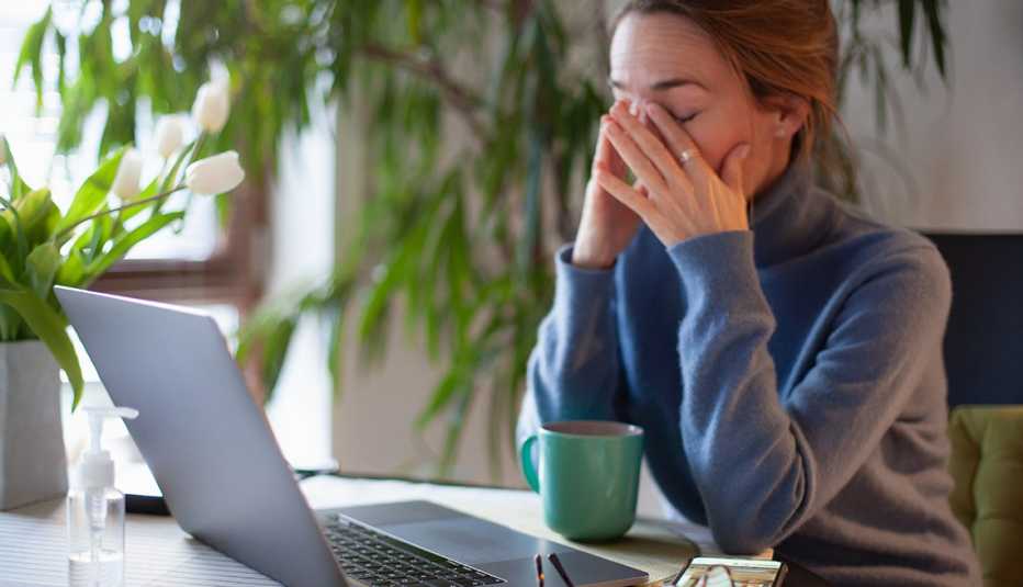Una mujer sentada frente a su computadora se frota los ojos en señal de cansancio