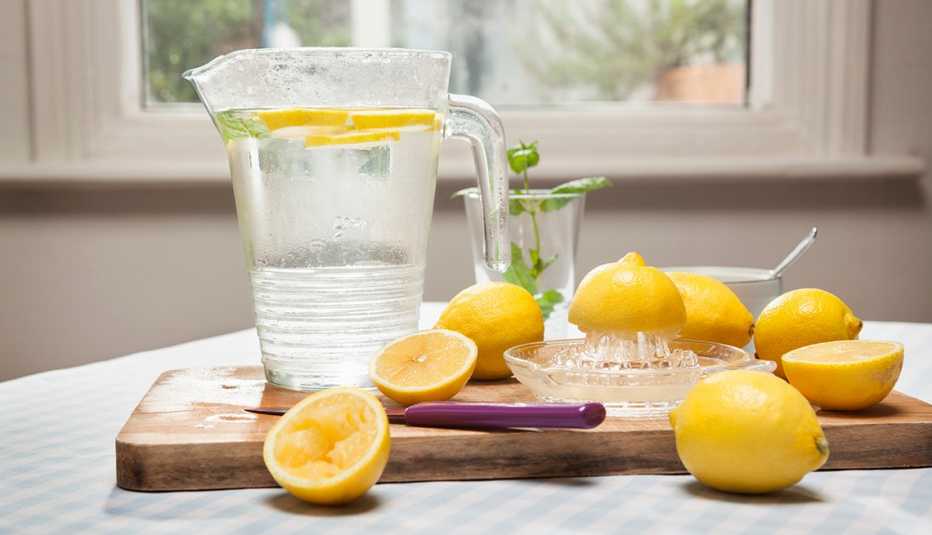 Limones enteros y cortados y una jarra de agua con rebanadas de limón