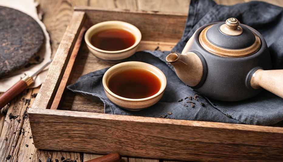 Una tetera y dos tazas de té en una bandeja de madera
