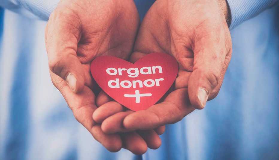 Manos juntas sostienen un corazón de papel que dice donante de órganos