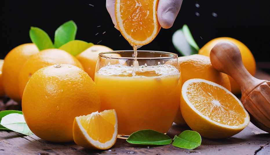 Un vaso donde recién exprimen una naranaja y naranjas enteras y cortadas alrededor