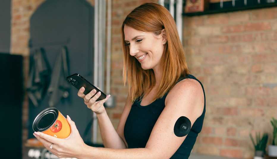 Una mujer, que usa un monitor de glucosa, usa su teléfono para corroborar los datos nutritivos de un producto enlatado