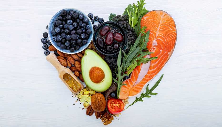 Alimentos saludables para el corazón que forman un corazón. Incluye arándanos, almendras, aguacate, aceitunas, frutos secos, salmón y vegetales