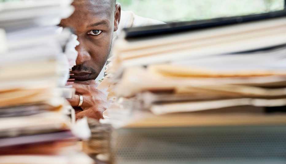 Frustrated Man At Work Sits Behind Piles Of Work, AARP Work, On The Job, What To Do If You Are Bullied At Work