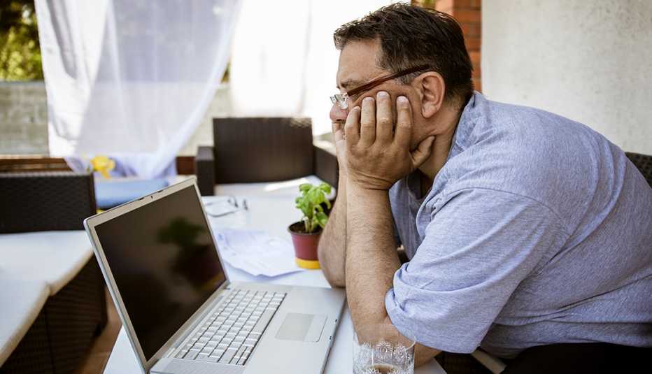 Hombre  apoya los codos sobre la mesa y con sus manos sostiene su cabeza mientras ve un curso en su computadora.