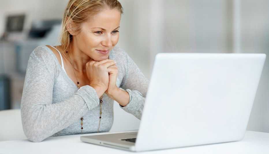 Mujer con expresión de felicidad mientras mira una computadora.
