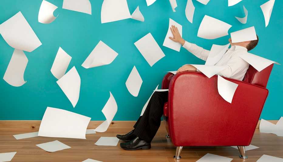 Hombre sentado en una silla roja con decenas de hojas de papel en el aire, quizás aprendiendo las nuevas reglas de la carta de presentación.