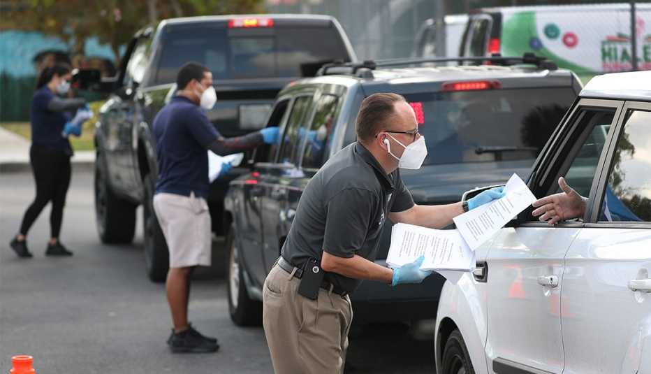 Eddie Rodriguez (derecha) y otros empleados de la Ciudad de Hialeah, Florida, reparten aplicaciones de desempleo a personas en sus vehículos. 