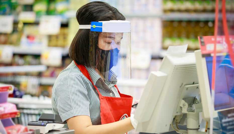 Trabajadora en la caja registradora de un almacén con mascarilla y visor protector