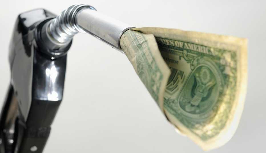 Distribuidor de gasolina con un billete de dólar saliendo del extremo de distribución, y ojo cuánto gastas en gasolina.